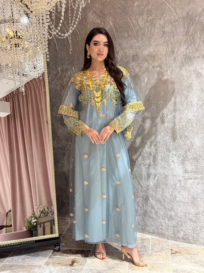 Woman in a dusty blue dress with gold Embroidered Kaftan standing in front of a mirror.