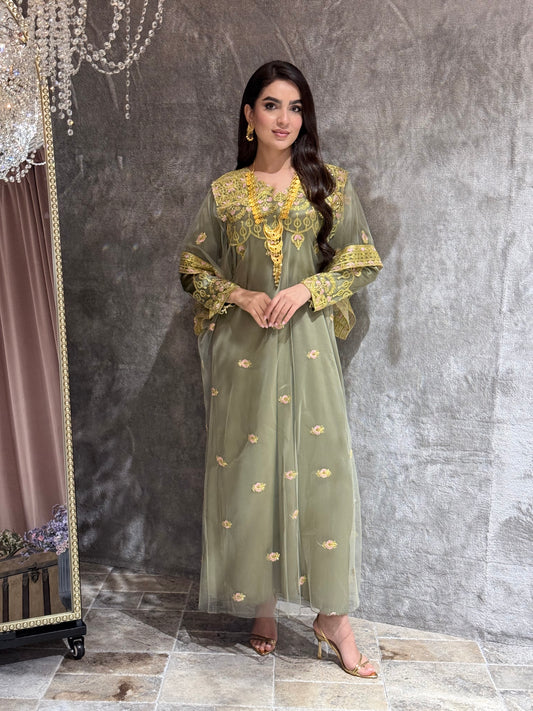 Woman in a green and gold embroidered kaftan outfit on a textured gray background