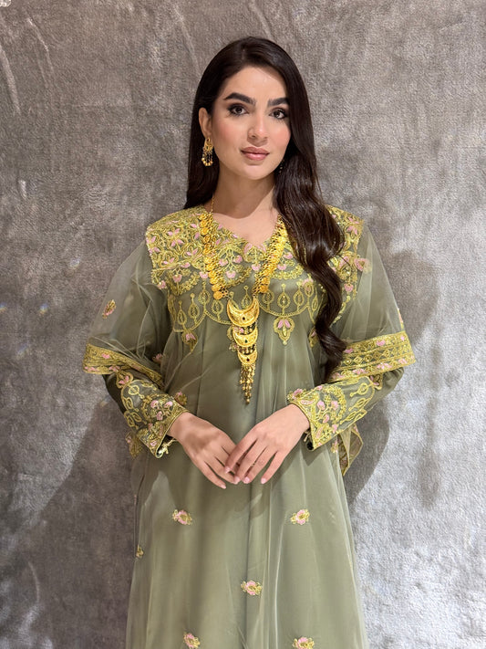 Woman in a green and gold embroidered kaftan outfit on a textured gray background