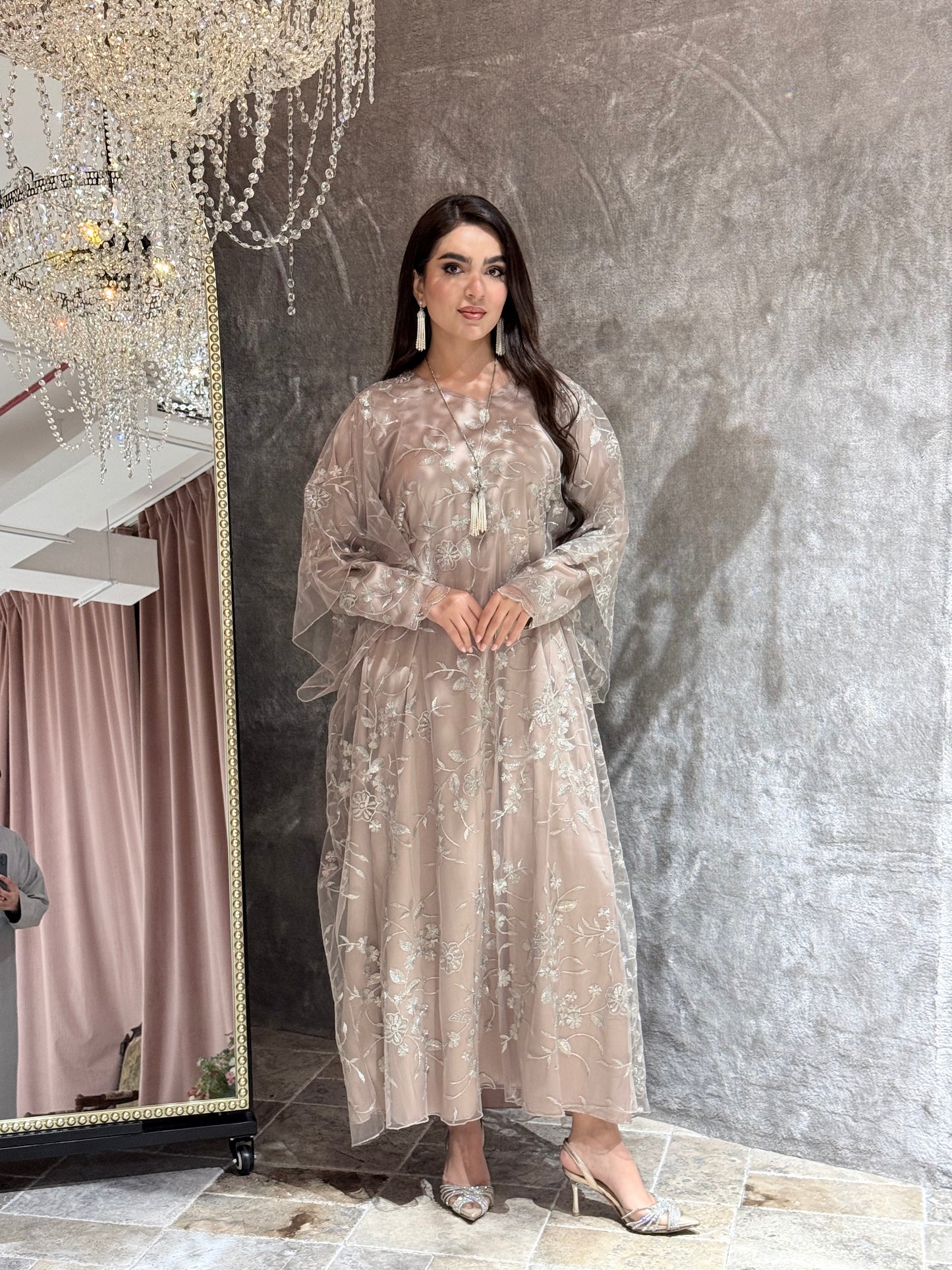 Woman in a Dusty Beige Floral Embroidered Kaftan standing in front of a mirror with a chandelier in the background