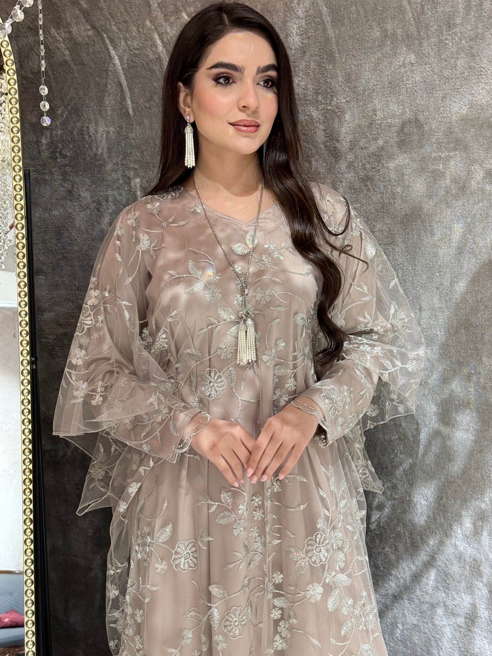 Woman in a Dusty Beige Floral Embroidered Kaftan standing in front of a mirror with a chandelier in the background