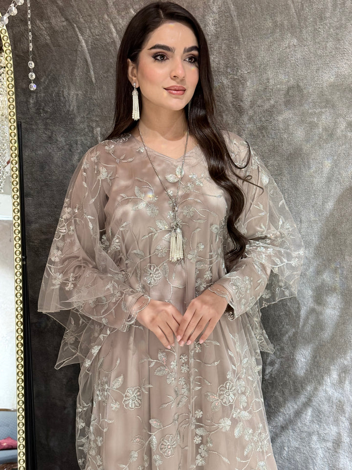 Woman in a Dusty Beige Floral Embroidered Kaftan standing in front of a mirror with a chandelier in the background