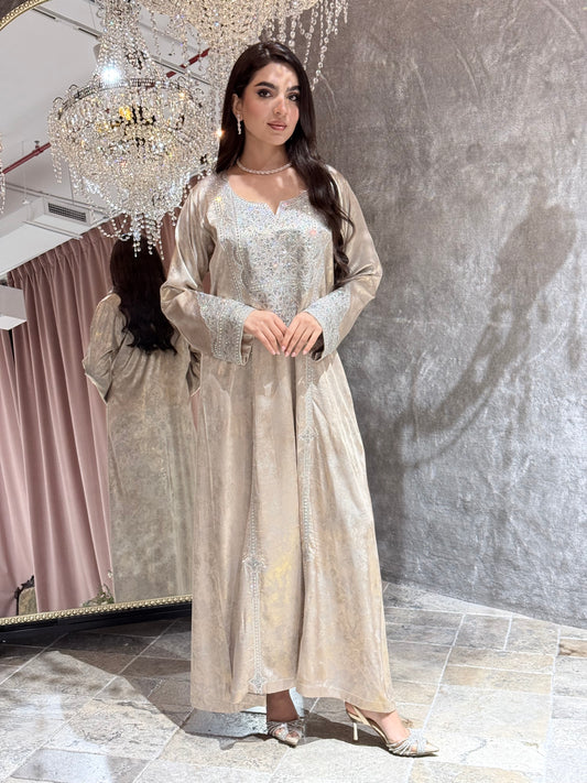 Woman in a long, elegant Beige Metallic Kaftan dress standing in a room with a chandelier.