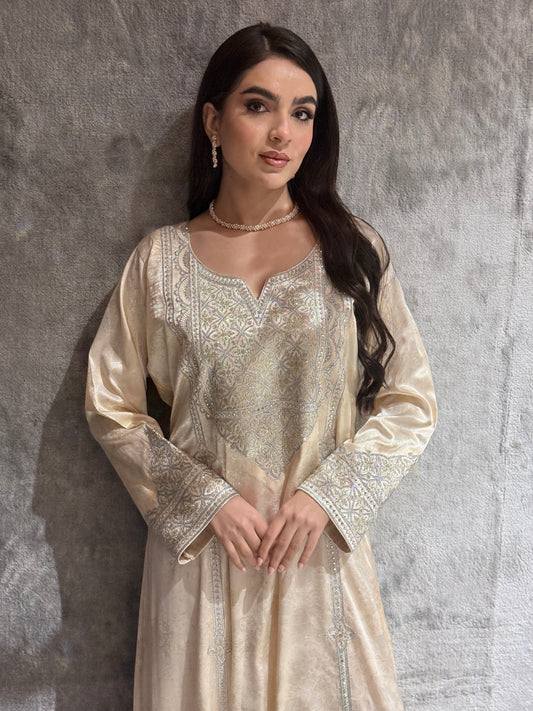 Woman in a Cream Metallic Luxury Kaftan dress standing on a gray textured surface