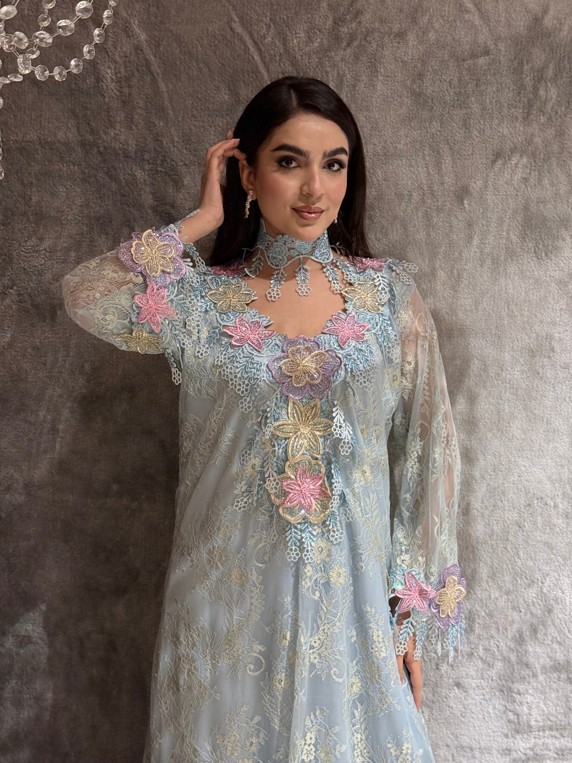 Woman wearing a O 284 Baby Blue Floral Lace Luxury Kaftan dress on a textured gray background
