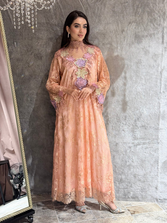 Woman wearing a peach evening kaftan with floral embellishments in a mirror reflection.