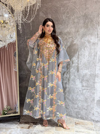 Woman in a grey luxury floral embroidered kaftan dress standing against a textured wall.