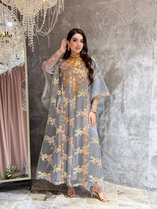 Woman in a grey luxury floral embroidered kaftan dress standing against a textured wall.