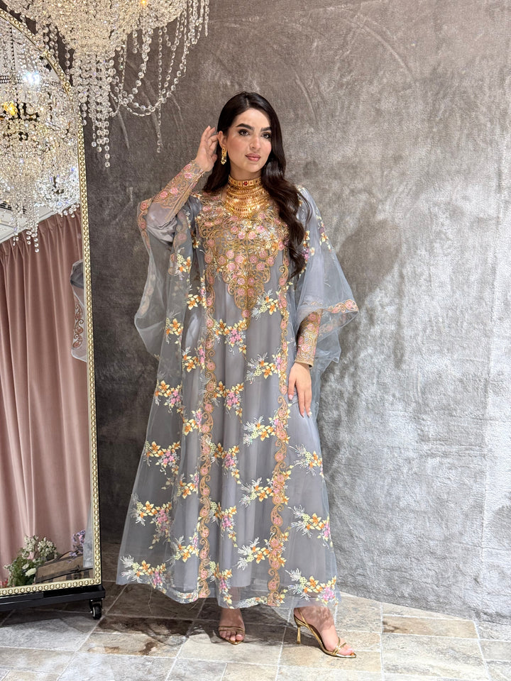 Woman in a grey luxury floral embroidered kaftan dress standing against a textured wall.