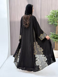 a woman wearing an elegant open-front black abaya featuring intricate multi-colored beadwork, sequins, and metallic embroidery in an indoor setting.