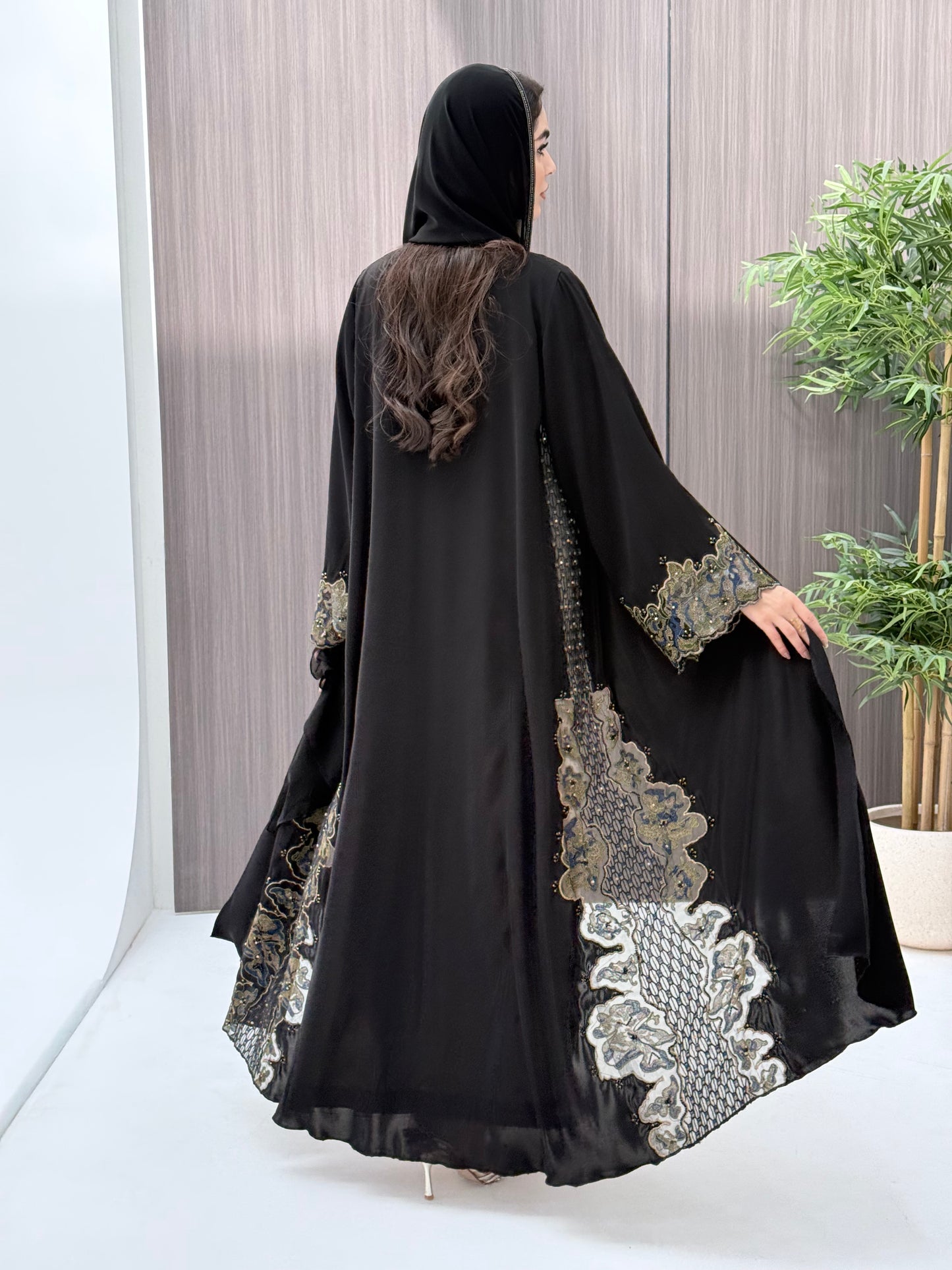 a woman wearing an elegant open-front black abaya featuring intricate multi-colored beadwork, sequins, and metallic embroidery in an indoor setting.