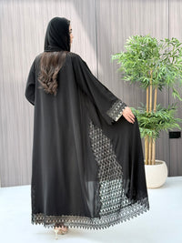 a woman wearing a sophisticated luxury open-front black abaya featuring intricate geometric sheer embroidery, elegant lace details, and beaded trims. Includes a matching sheila on a patterned background