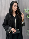 a woman wearing a sophisticated luxury open-front black abaya featuring intricate geometric sheer embroidery, elegant lace details, and beaded trims. Includes a matching sheila on a patterned background