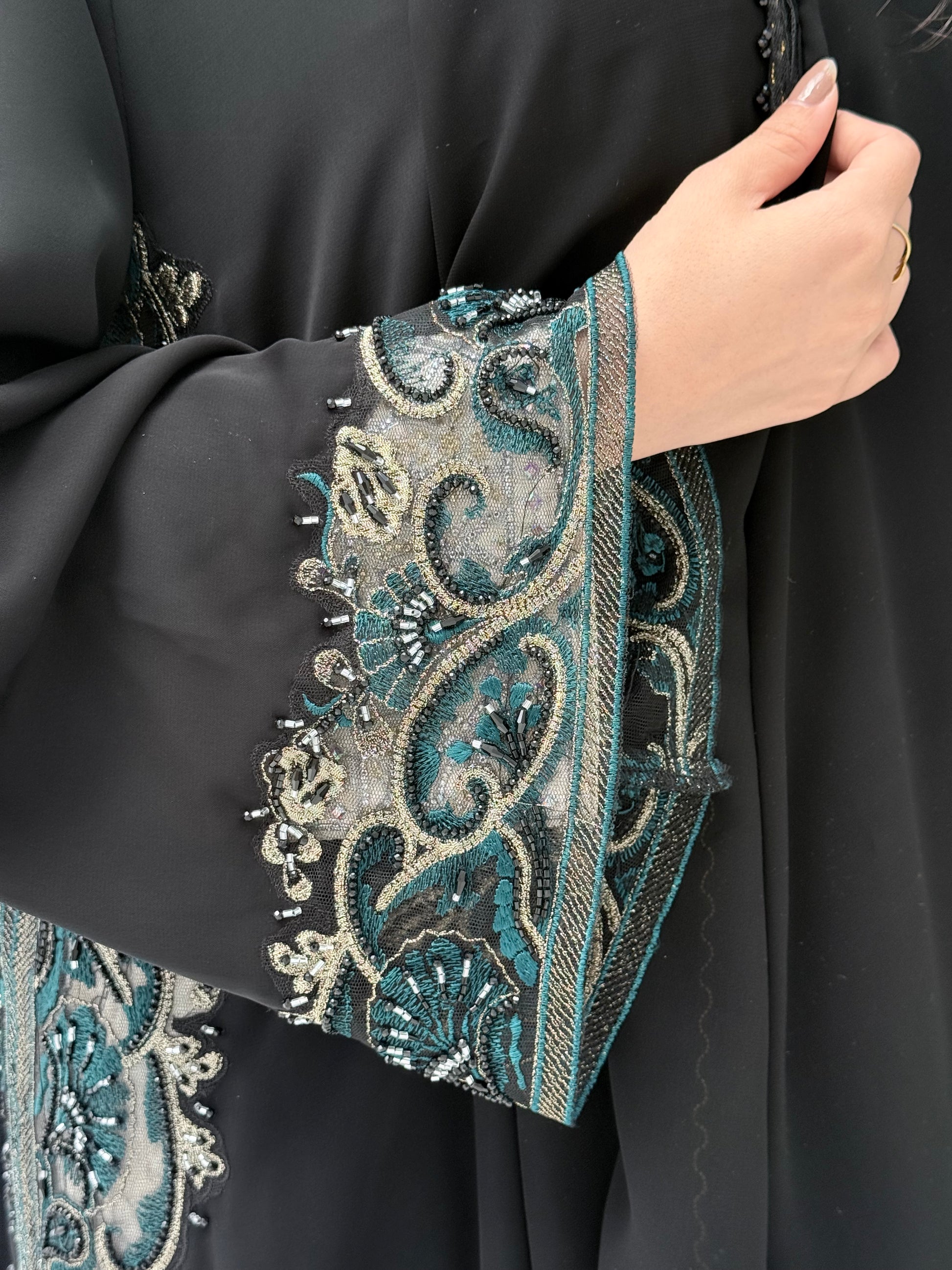 Close-up of woman wearing a black nida fabric abaya with intricate blue and silver embroidery