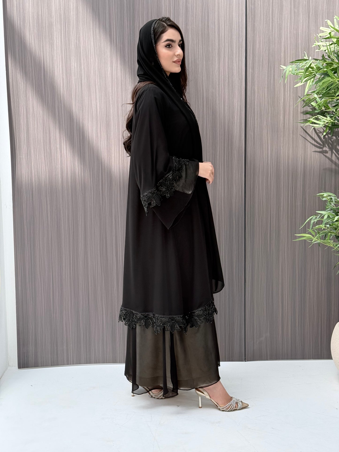 Woman wearing a black abaya standing on a wooden floor.