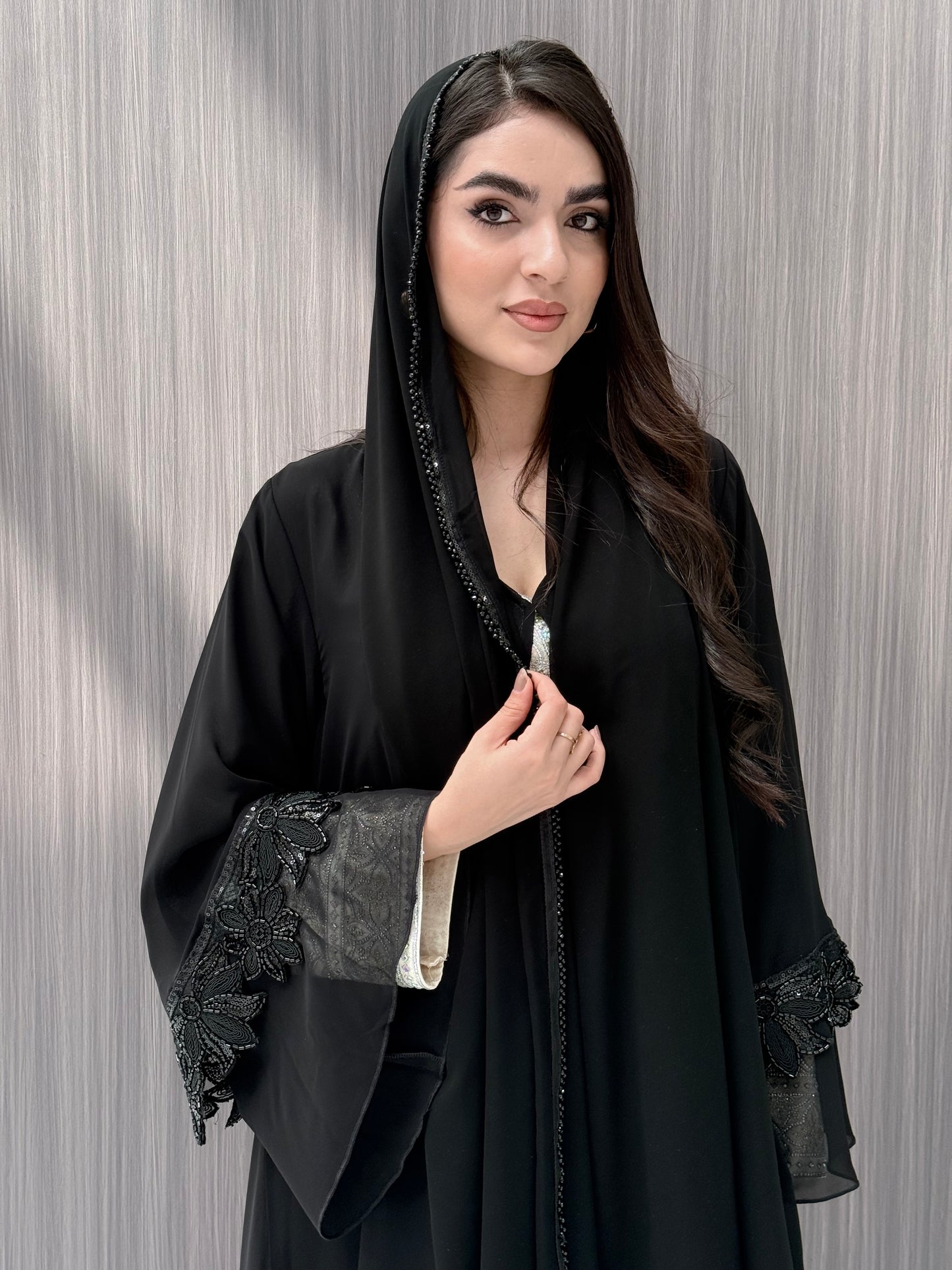 Woman wearing a Black Beaded Floral Open Front Abaya with matching sheila on a  gray background