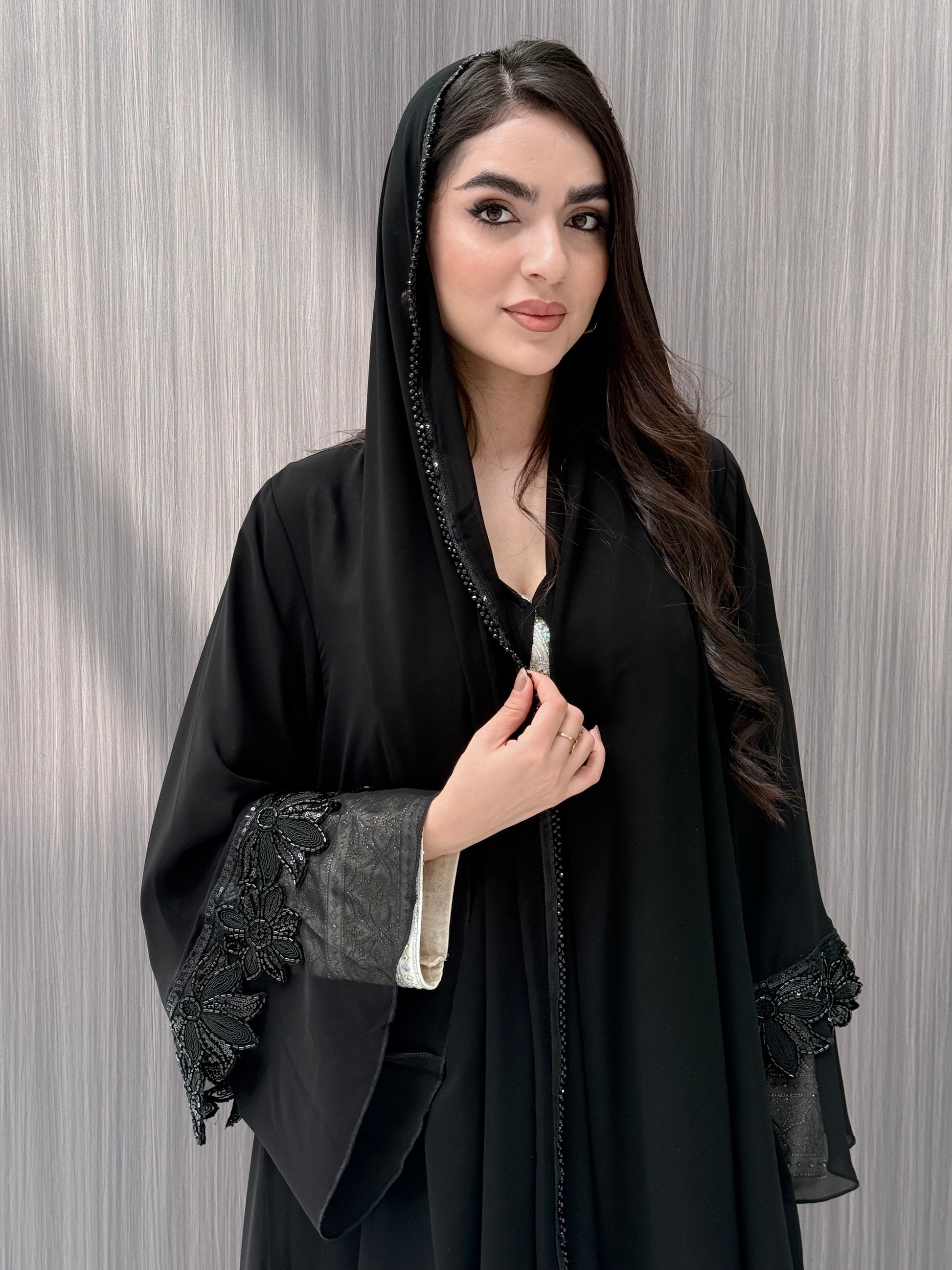 Woman wearing a Black Beaded Floral Open Front Abaya with matching sheila on a  gray background