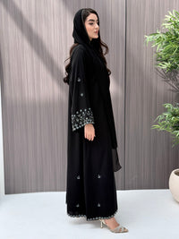 A woman wearing a black embroidered floral open abaya, which is perfect for ceremonies, Eid, and parties.