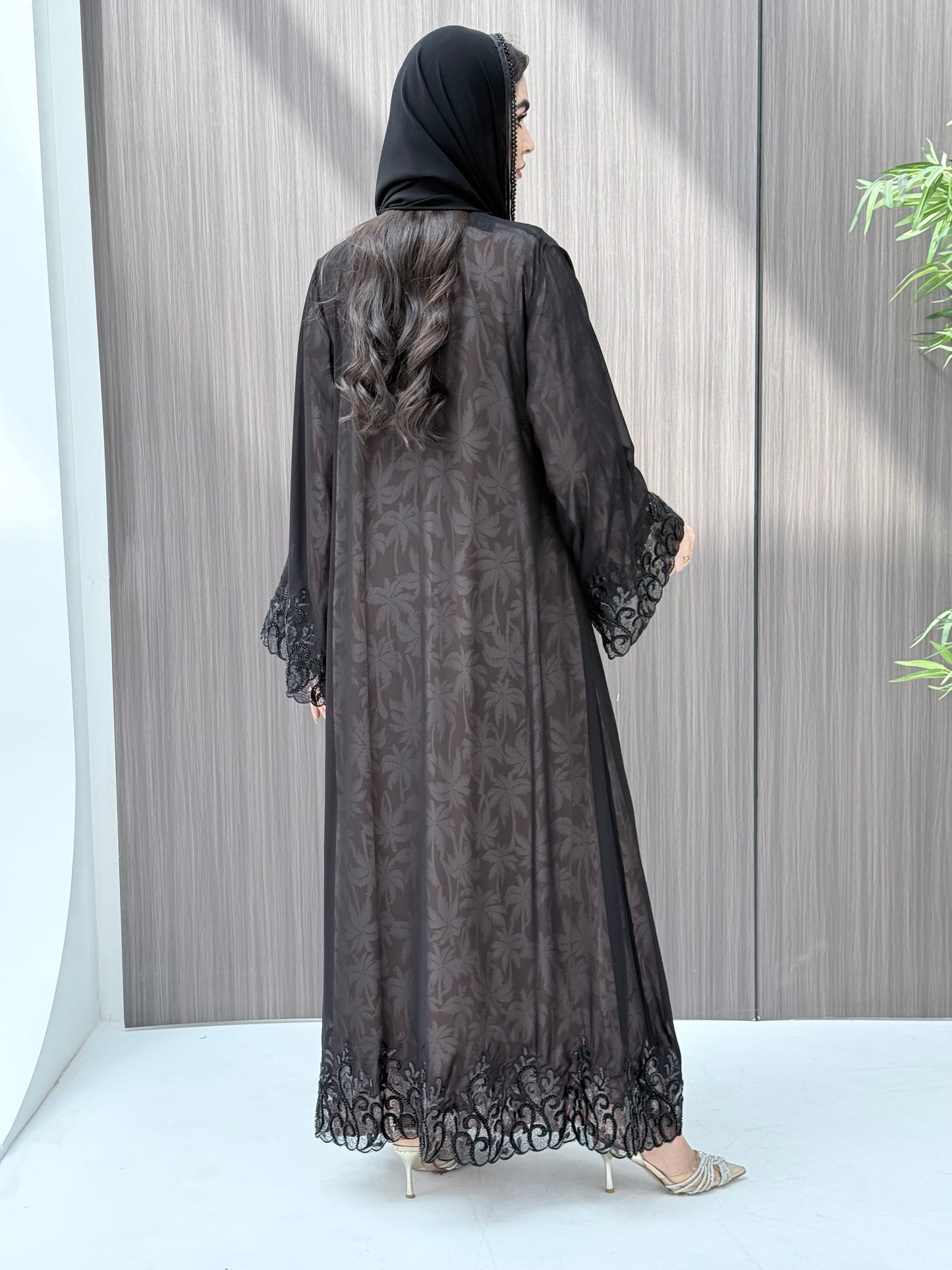 Woman wearing an open-front sheer black abaya with a matching beaded sheila on a gray background