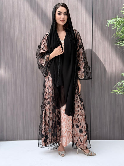 Woman wearing a Black Sheer Floral Appliqué Open Front Abaya with a mathcing sheila against a wooden panel background