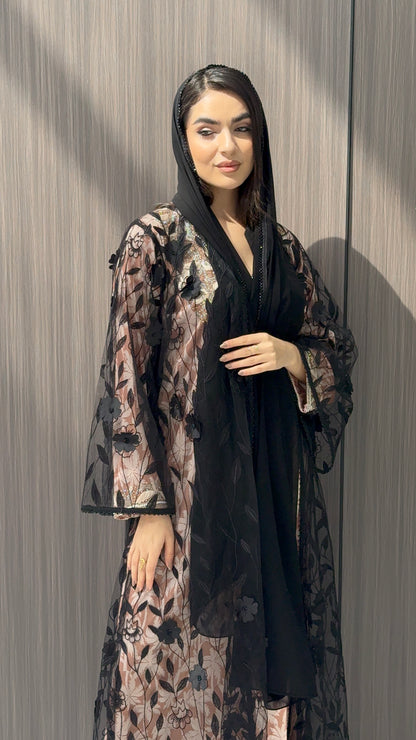 Woman wearing a Black Sheer Floral Appliqué Open Front Abaya with a mathcing sheila against a wooden panel background