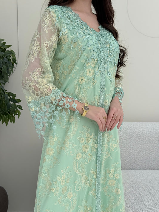 A woman wearing a mint green floral lace kaftan, perfect for Eid, luxury occasions and parties.