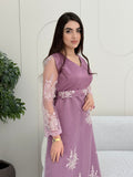 Woman in an elegant dusty purple modest jalabiya designed with a flattering V-neck, floral embroidered sheer sleeves, and a beautifully structured matching waist belt. standing against a white wall.